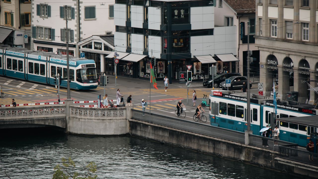 The Art of Drawing Readers In: Your attractive post title goes here A bustling scene in Zürich featuring trams, cyclists, and pedestrians crossing a bridge.