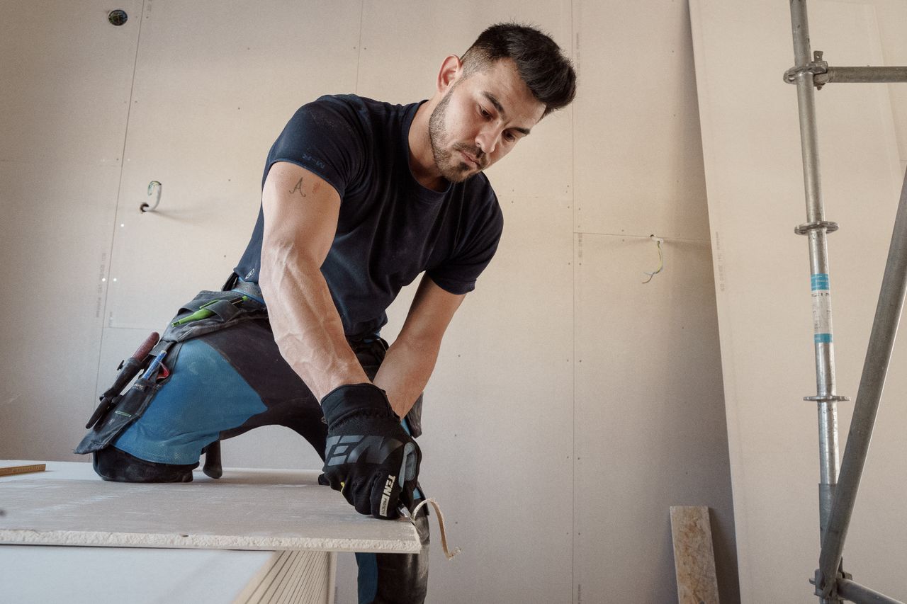team-01 Man in gloves cutting plasterboard for drywall installation inside a building.